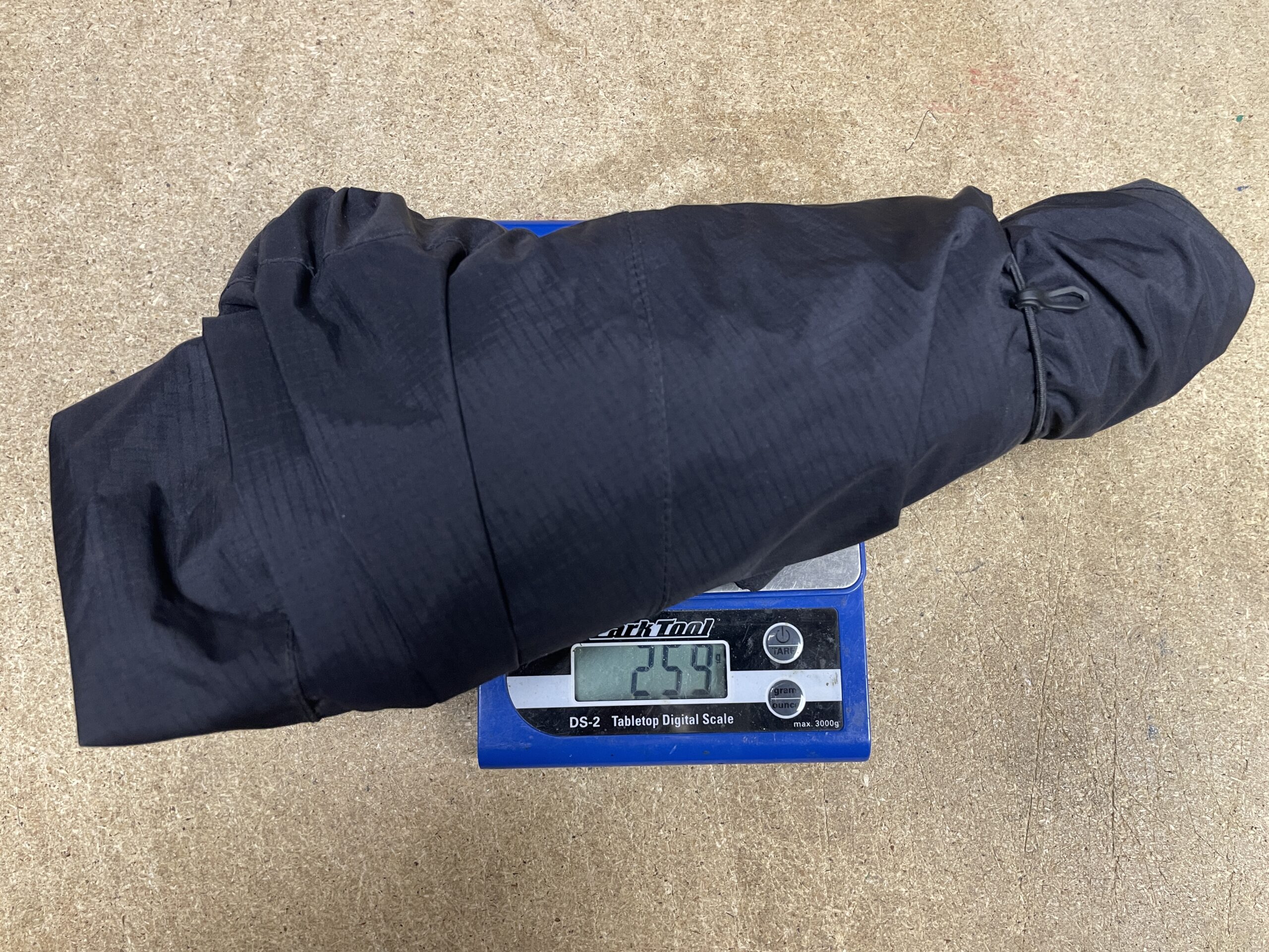 A compact, rolled black jacket resting on a digital scale, displaying a weight of 259 grams.