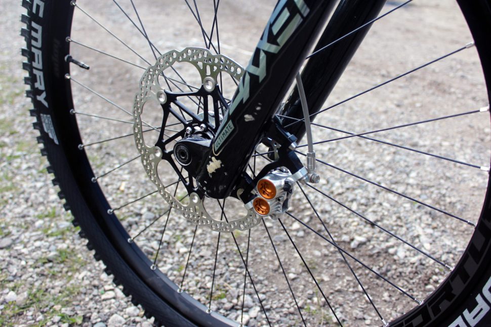 Close-up view of a bike's front wheel, showcasing the disc brake and spokes on a gravel surface.