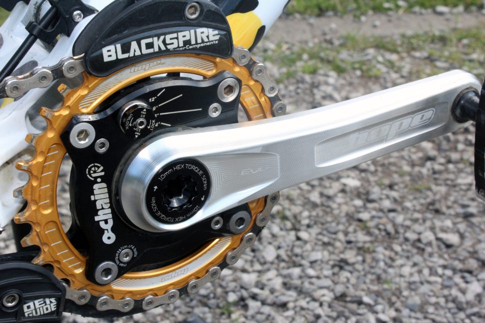Close-up of a mountain bike crankset featuring a silver crank arm and a golden chainring with the 'Blackspire' logo visible.
