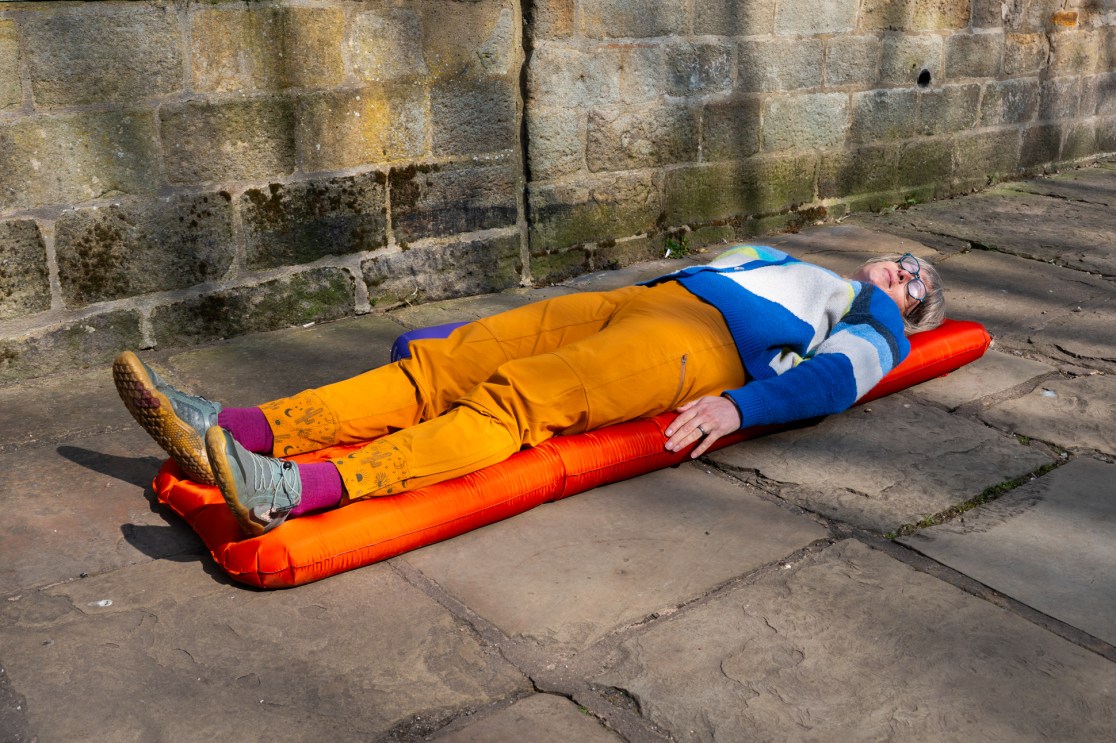 Person lying on an orange inflatable camping mat on a stone surface, wearing colorful outdoor clothing.