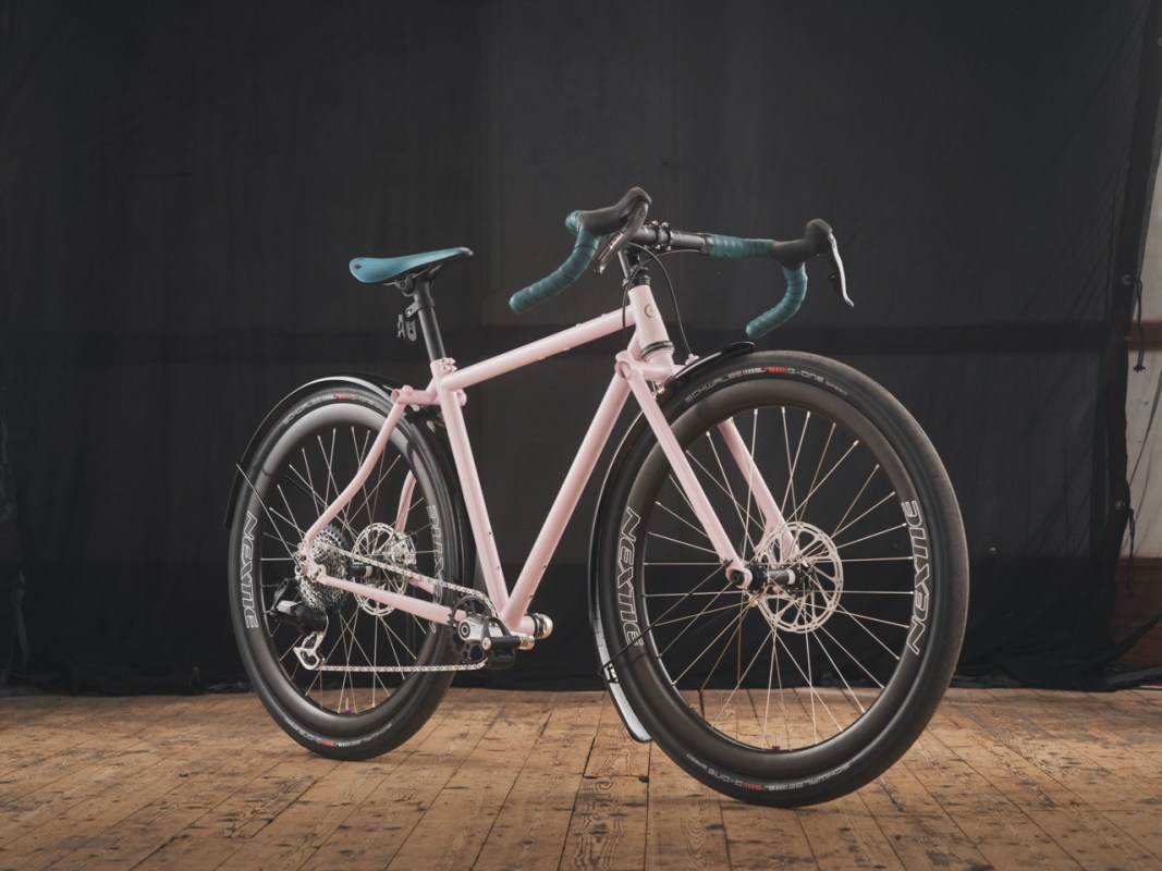 A pink bicycle with a sleek design, featuring drop handlebars and disc brakes, set against a dark background.