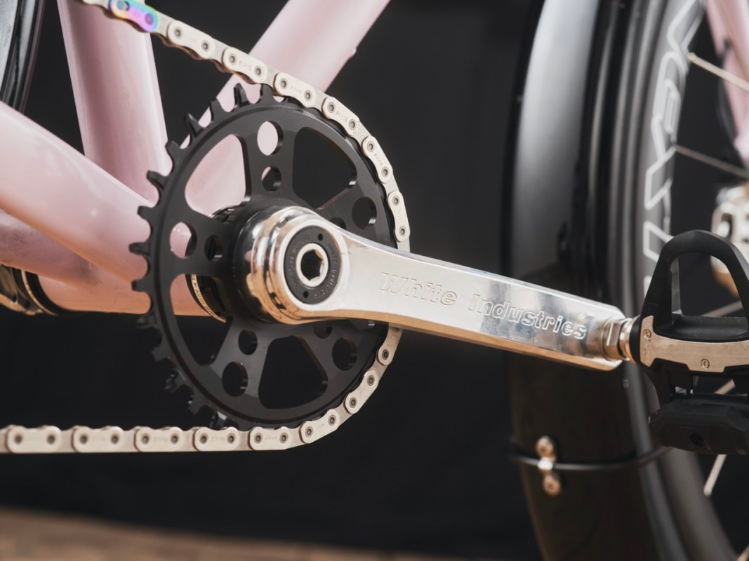 Close-up of a bicycle crankset featuring a black chainring and a polished silver crank arm with 'White Industries' engraved, set against a dark background.