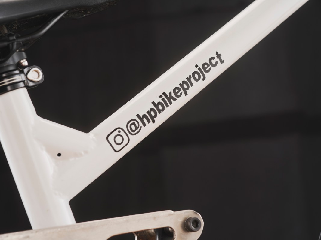 Close-up of a white bicycle frame featuring the Instagram handle '@hpbikeproject' printed on the side, showcasing a detailed view of the tubing and components.