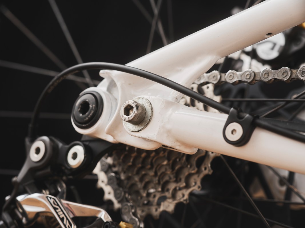 Close-up view of a white bicycle frame's bottom bracket and rear suspension components, highlighting the intricate design and cable routing.