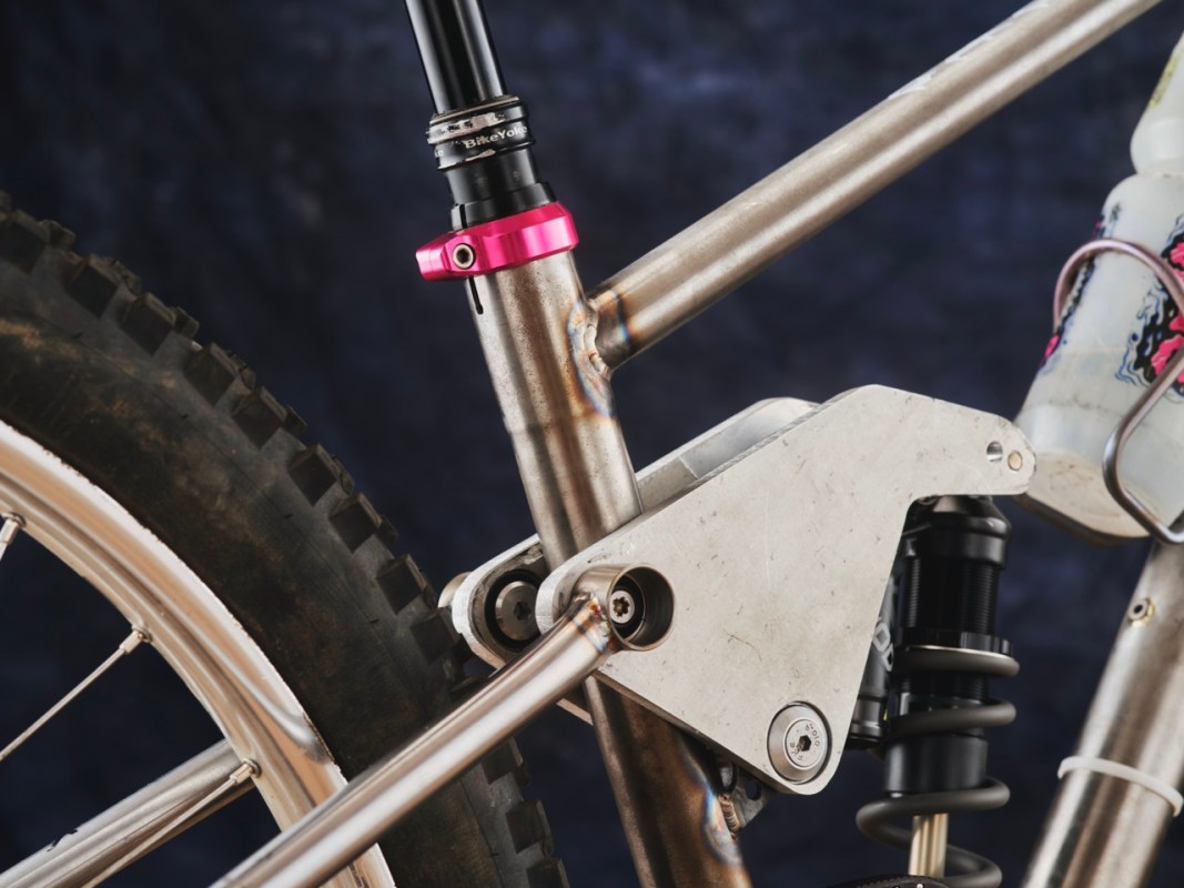 Close-up view of a custom bike frame featuring a metallic structure, with a pink adjustment ring on the shock absorber, showcasing the suspension system and linkage mechanism.