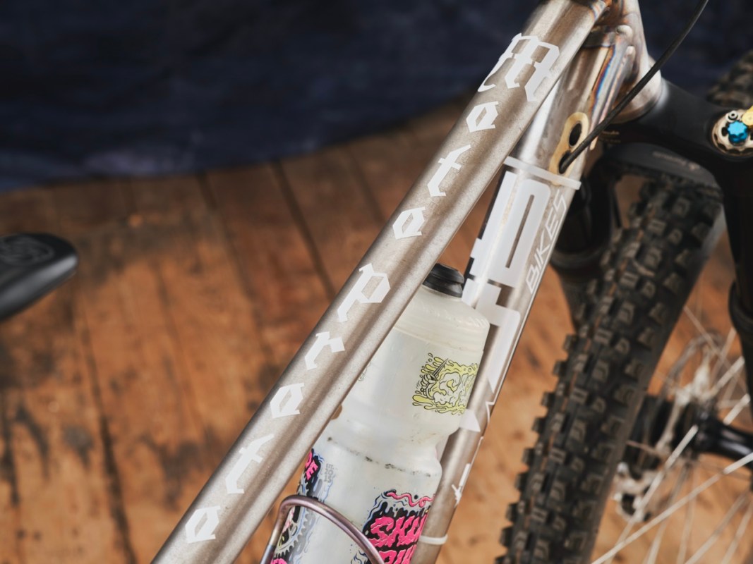 Close-up of a mountain bike frame showing the brand name and details on the top tube, with a water bottle mounted on the frame.