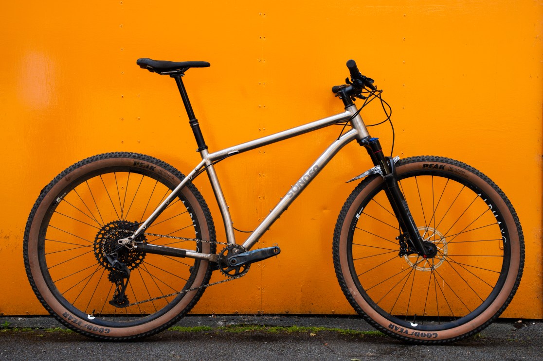 Side view of a Sonder Broken Road Ti hardtail mountain bike against an orange background.