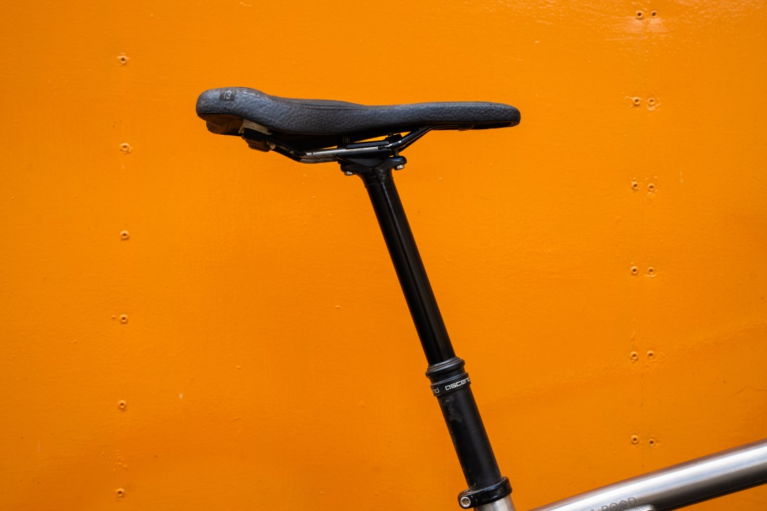 Close-up of a bicycle seat and dropper post against an orange background.