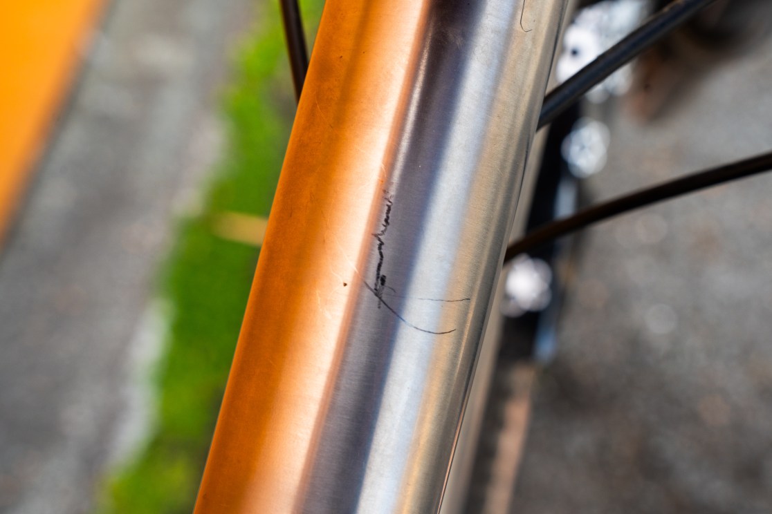 Close-up view of a scratched titanium frame of a mountain bike, showing a visible mark and wear on the tubing.