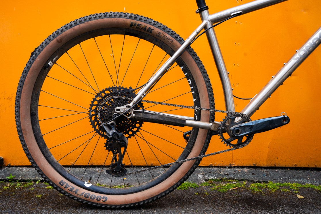 Detail shot of the rear drivetrain and wheel of a Sonder Broken Road Ti mountain bike against an orange background.