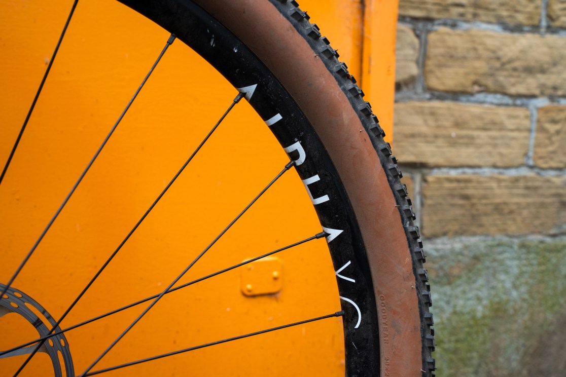 Close-up of a bicycle wheel showing the Goodyear Peak Ultimate tire and Sonder Alpha rim against an orange background.