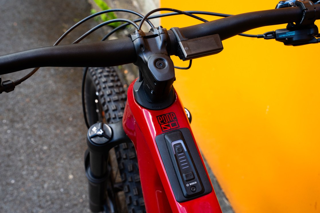 Close-up view of the handlebars, display, and top tube of a Merida E160 electric bike against an orange background.