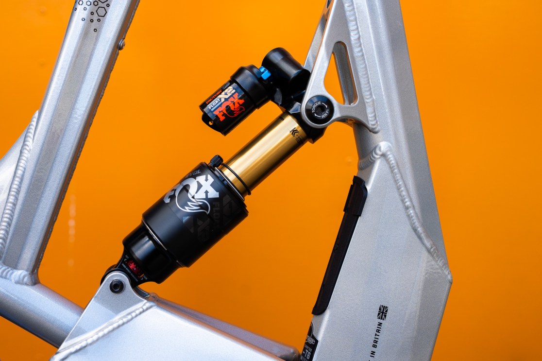 Close-up of a silver bike frame featuring a FOX Float X2 shock absorber against an orange background.