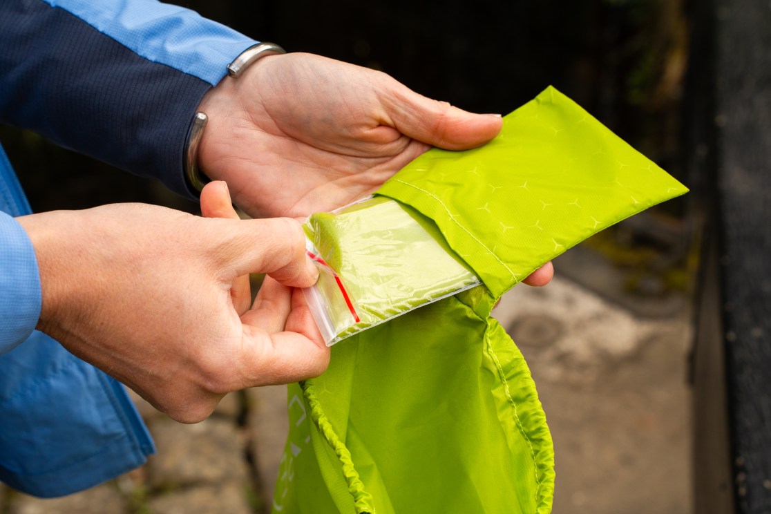 A person holding a bright green storage sack with a small ziplock bag visible inside, showcasing the contents.