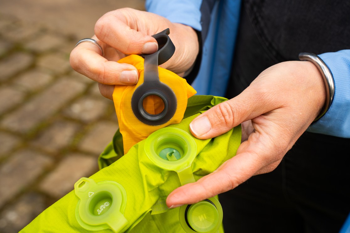 A person holds a green camping mat with valves, showcasing the inflator and deflator components.