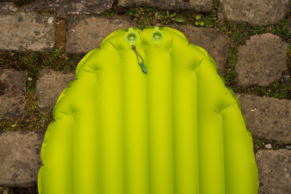 Close-up view of a bright green inflatable sleeping mat featuring valves for inflating and deflating, placed on a stone surface.