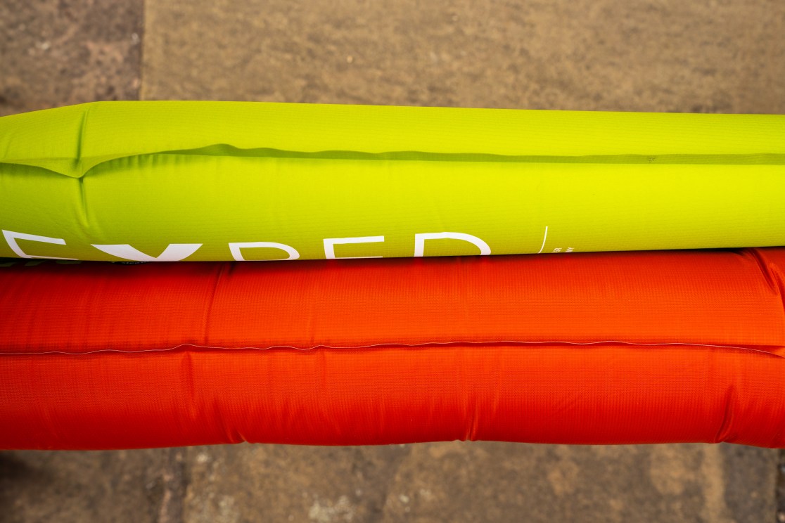 Close-up view of an Exped Ultra 5R sleeping mat in green positioned above a Big Agnes Rapide SL sleeping mat in orange.