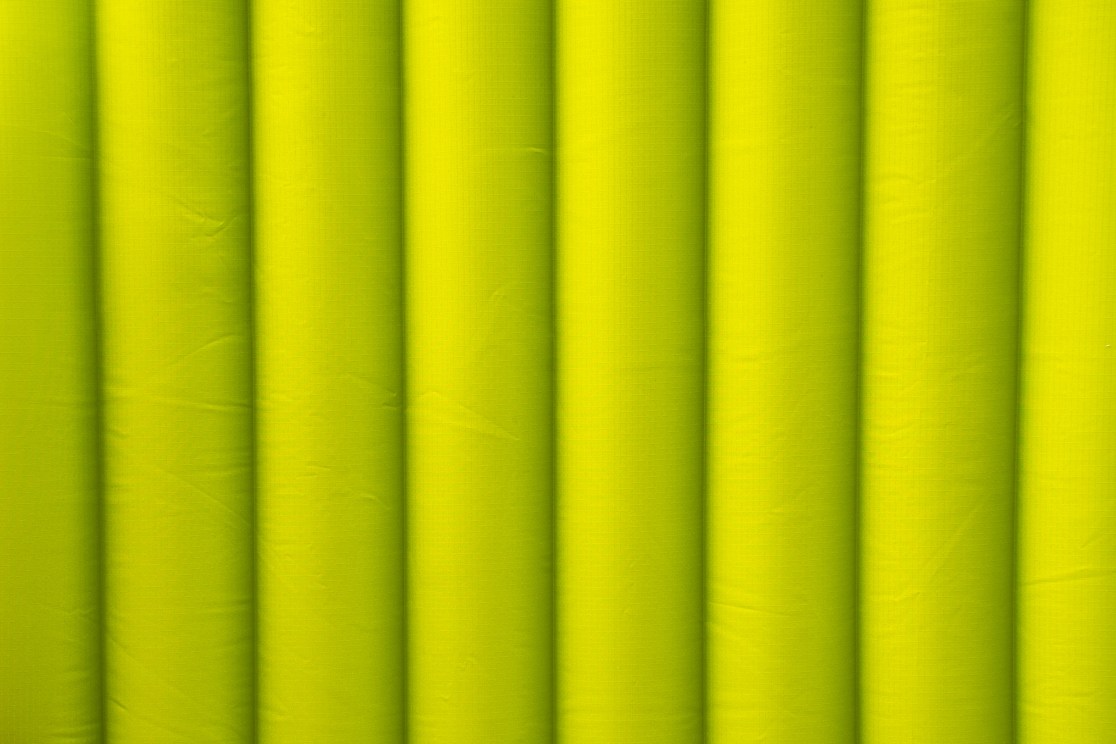 A close-up image of several insulated sleeping mats, featuring a textured surface in bright green, arranged closely together.