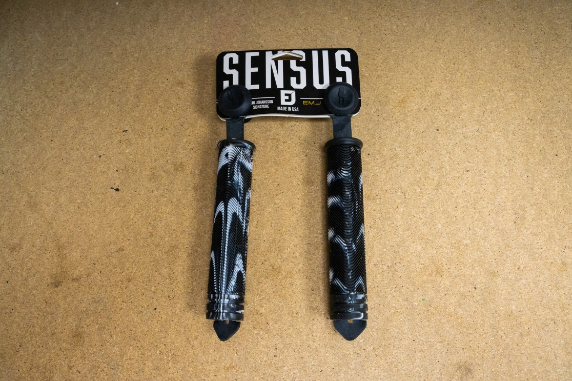 Sensus EmJ signature grips displayed on a wooden surface, featuring a black and white design with a textured grip surface.