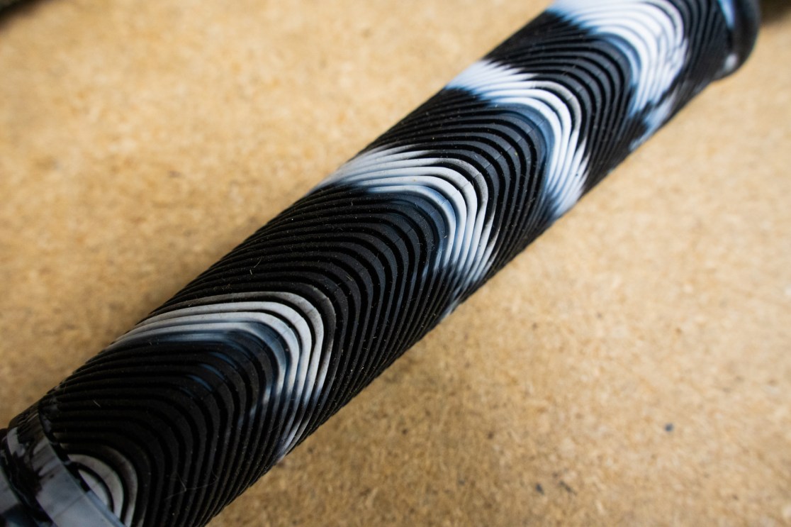 Close-up view of a textured bicycle grip featuring a wavy pattern, predominantly in black and white colors, placed on a wooden surface.