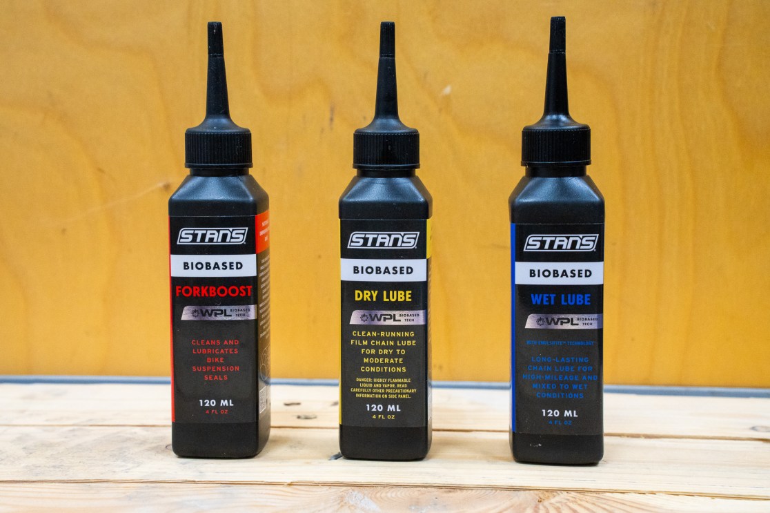 Three bottles of bike lubricant: Forkboost, Dry Lube, and Wet Lube, each 120 ML, arranged on a wooden surface.