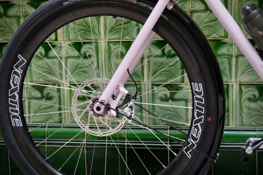 Close-up of a bike wheel featuring a disc brake and a wide tire, with 'NEXTIE' branding visible on the wheel rim.