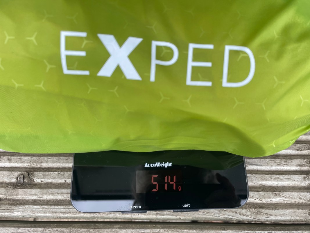 A green Exped storage bag placed on a digital scale displaying a weight of 514 grams, set on a wooden surface.