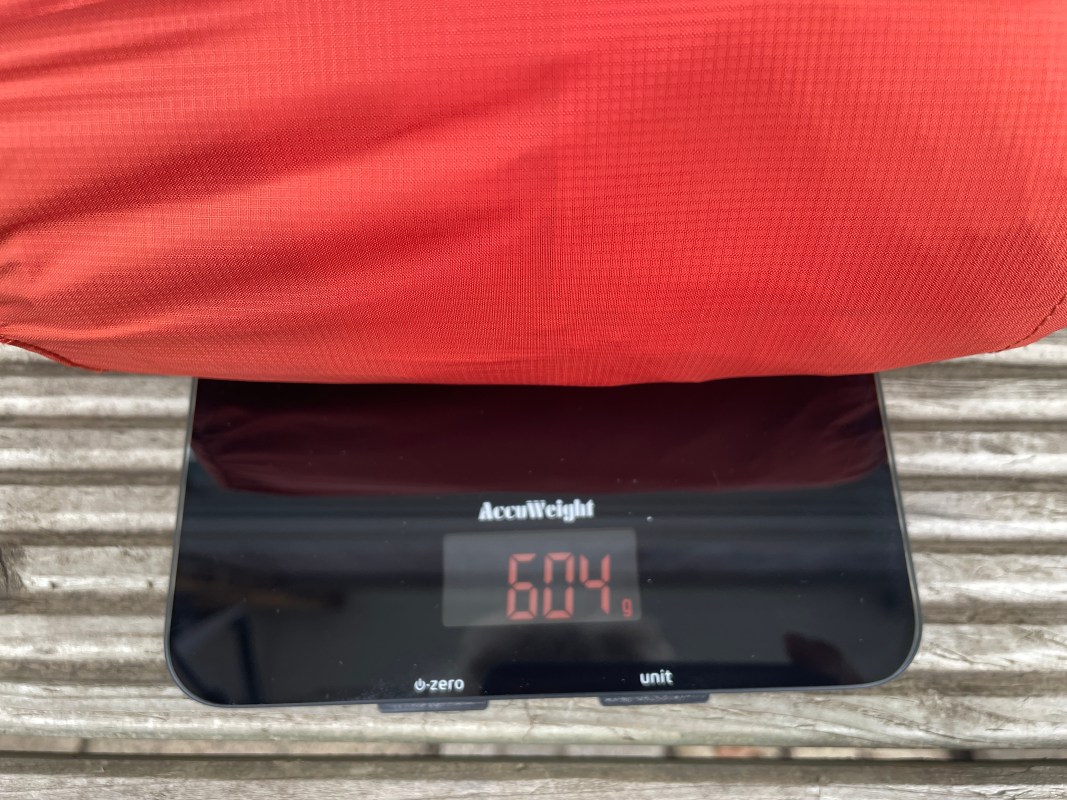 A red sleeping mat resting on a digital scale, displaying a weight of 604 grams.