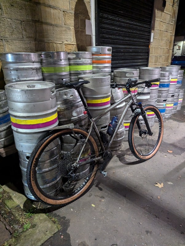 A Sonder Broken Road Ti mountain bike parked against a stack of metal beer kegs in an urban setting.