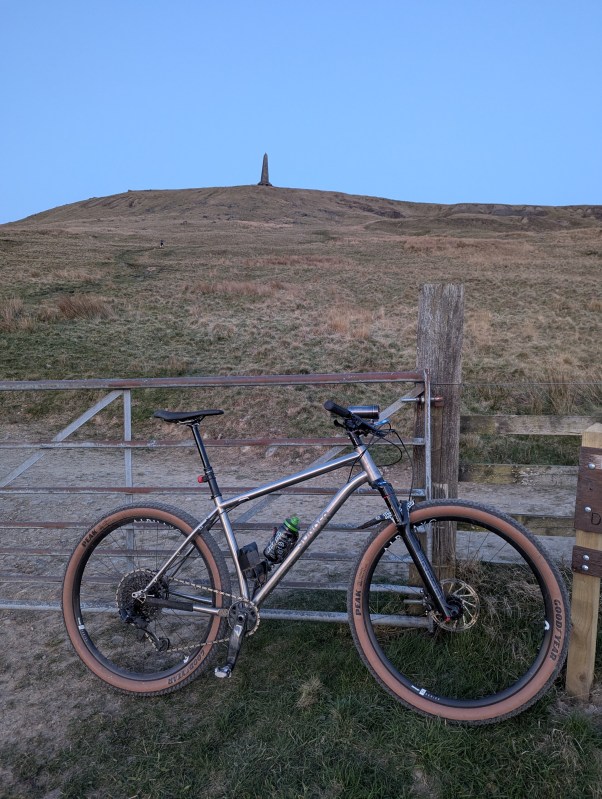 A Sonder Broken Road Ti mountain bike parked near a wooden fence with a hill and a monument in the background under a clear sky.
