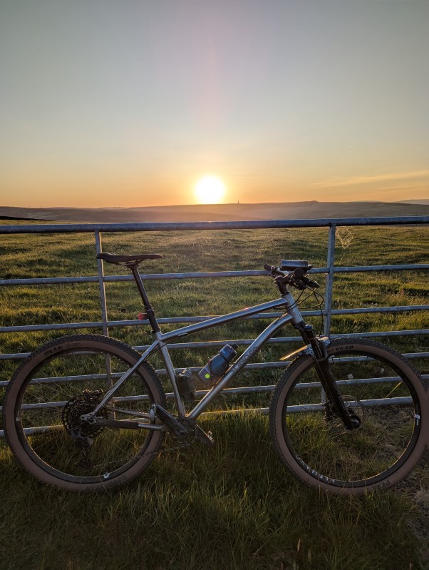 Sonder Broken Road Ti mountain bike parked in front of a sunset over a grassy landscape.