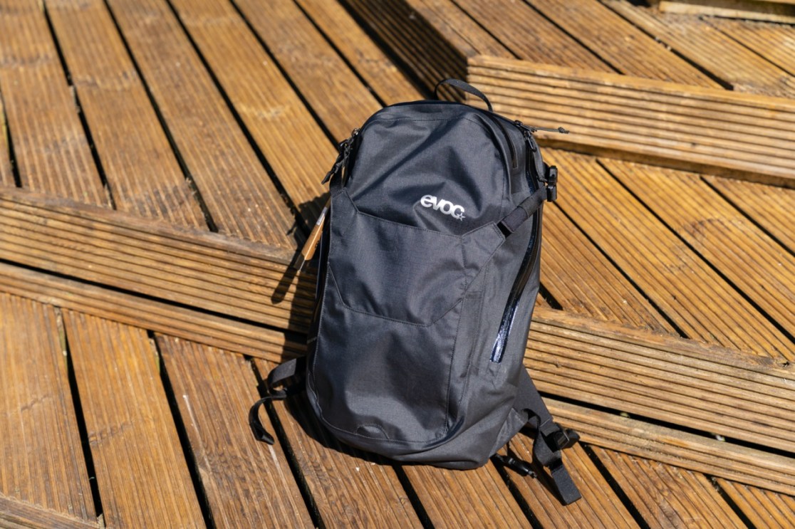 A black Evoc Allride 3D WP16 backpack displayed on wooden planks.