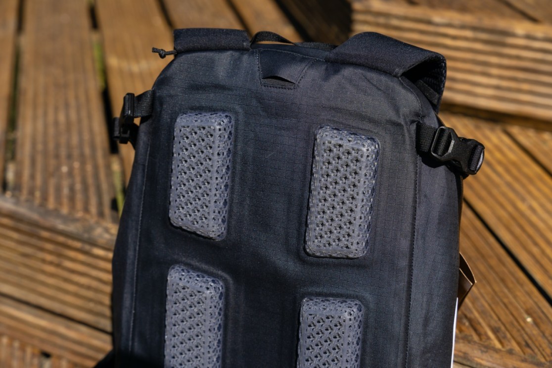Close-up of the back panel of the Evoc Allride 3D WP16 Backpack, featuring ventilation pads and adjustable straps against a wooden background.