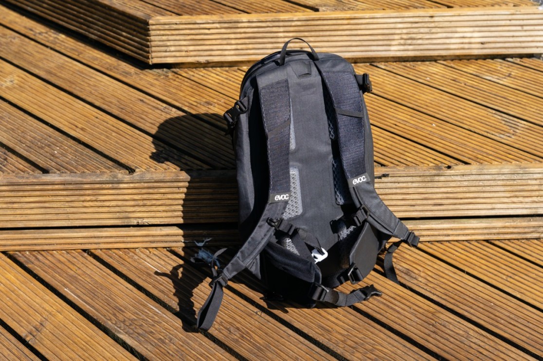 A black Evoc Allride 3D WP16 backpack, featuring a weatherproof design and 360-degree ventilation, resting on wooden boards.