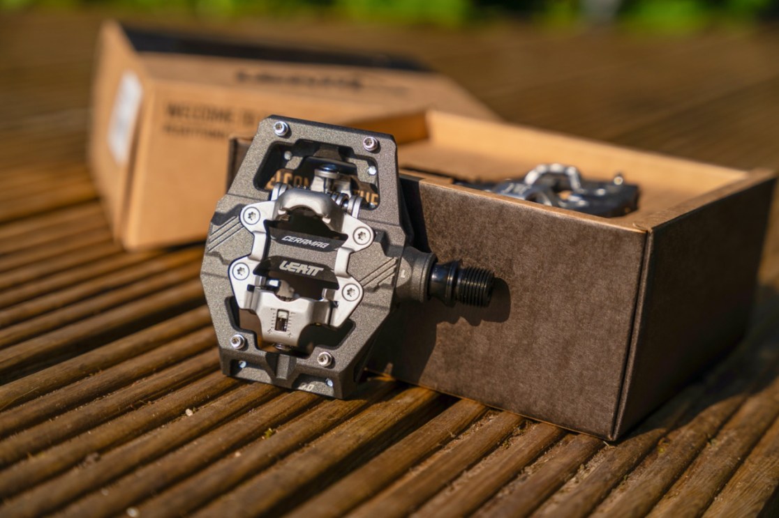 Close-up of a Leatt bike pedal on a wooden surface with a brown box in the background.