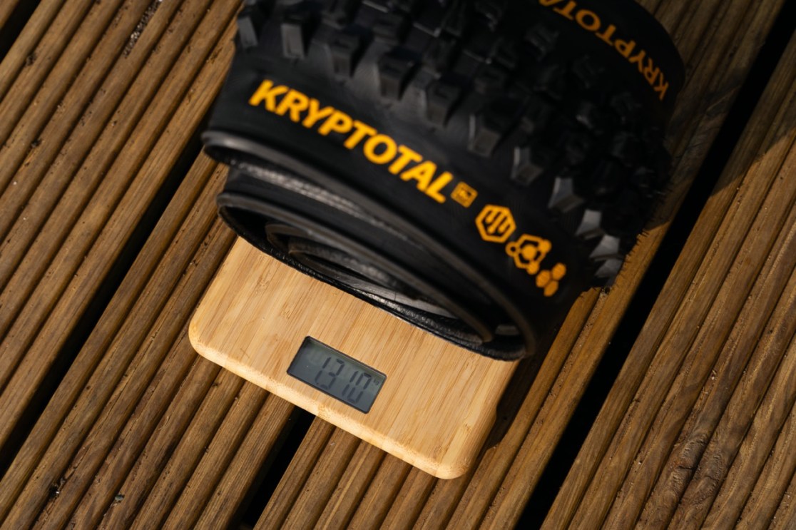 A close-up of a Kryptotal bike tire resting on a digital scale, displaying a weight of 1310 grams.
