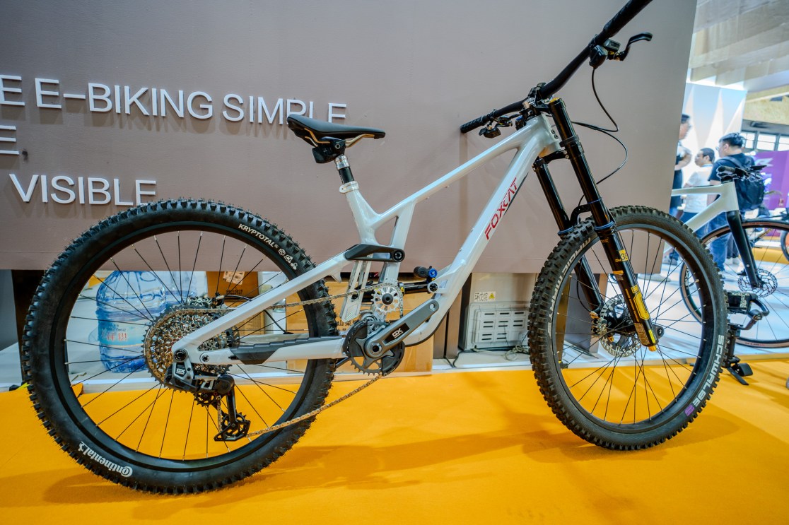 A white Foxcat prototype mountain bike displayed at the China Cycle Expo. The bike features a dual crown fork, fat tires, and a modern design, set against a brown background with promotional text.