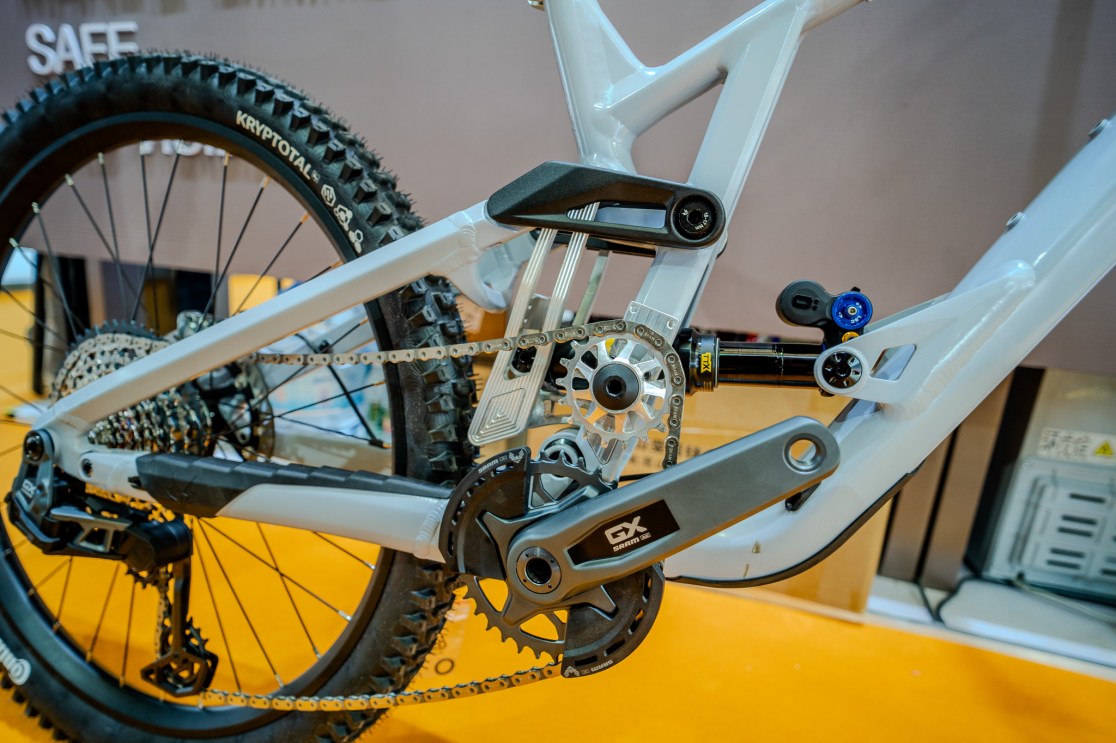 Close-up view of a mountain bike's drivetrain, showcasing the SRAM GX components, chain, and suspension linkage against an orange exhibition floor.