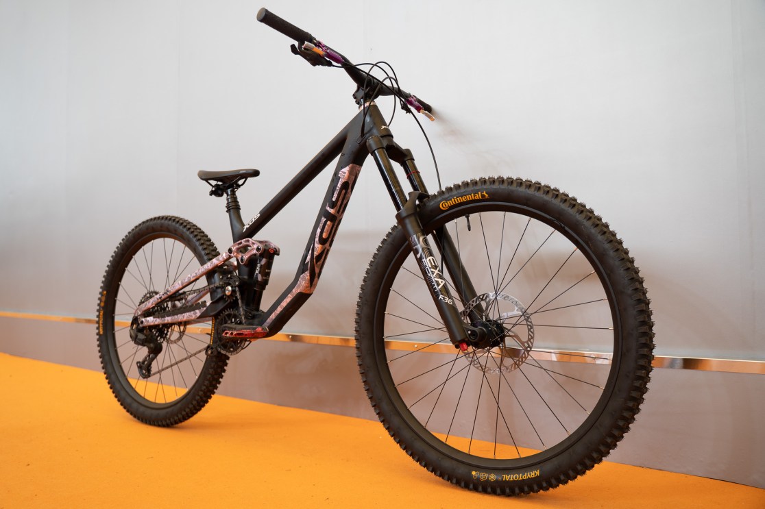 A black mountain bike displayed on an orange carpet, featuring a sturdy frame, thick tires, and a dual suspension system, showcasing innovative design elements.