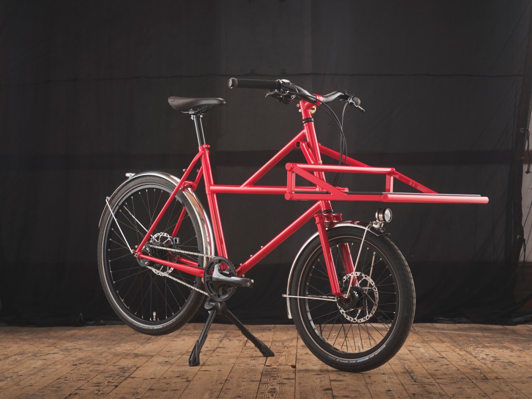 A vibrant red bike designed for cargo, featuring a unique frame with an extended rack, set against a dark backdrop.
