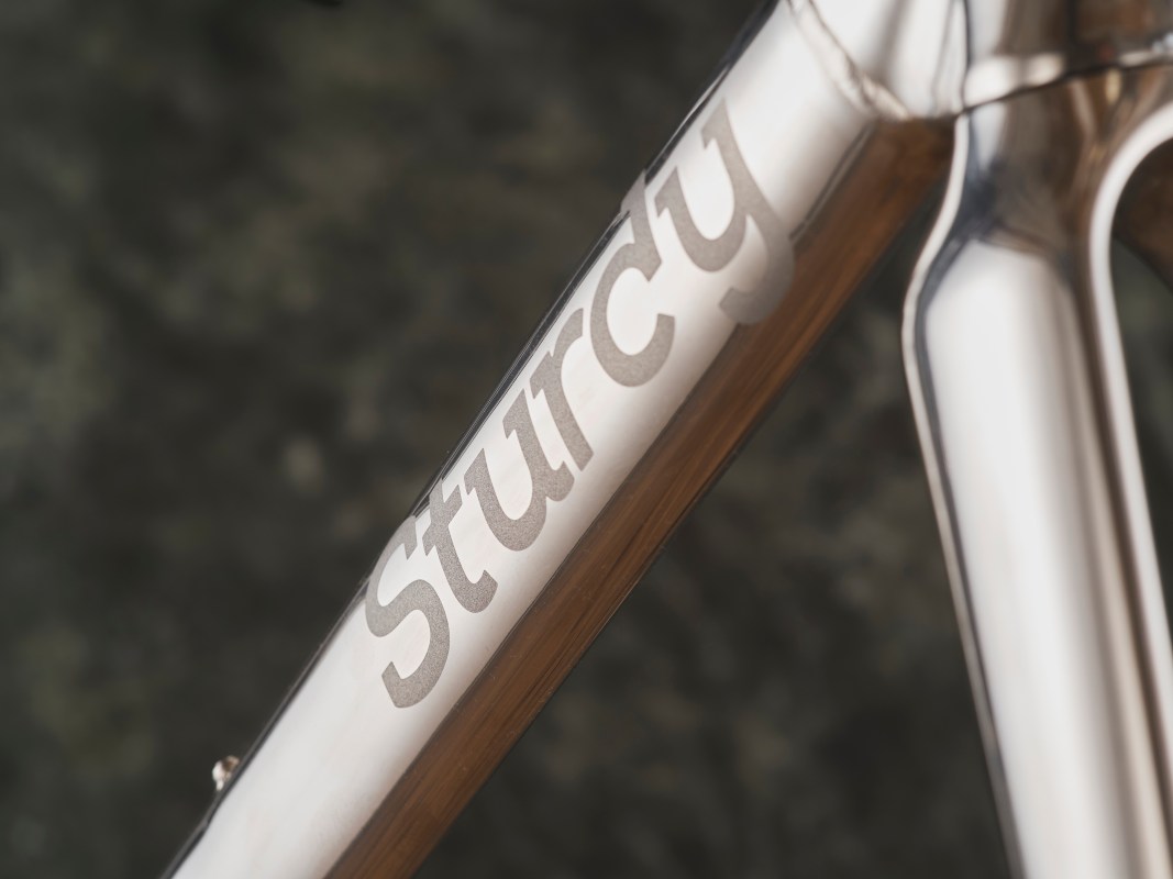 Close-up of a metal bike frame showcasing the engraved logo 'Sturcy' on the tubing.