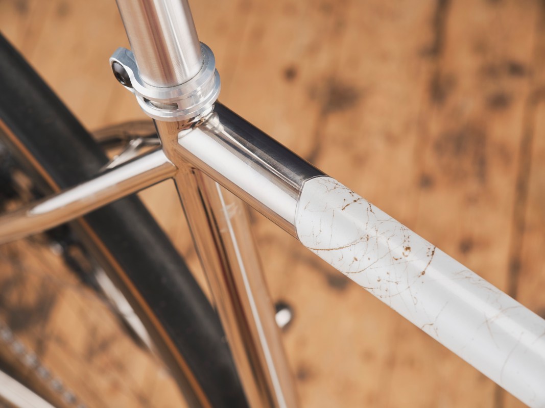 Close-up of a polished bike frame with a white paint section featuring a cracked design, set against a wooden floor.
