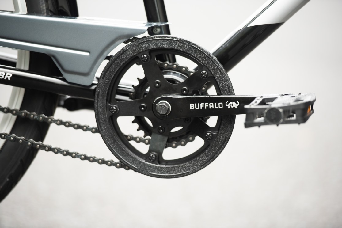 Close-up of a bicycle crankset and pedals, featuring a black chainring with the word 'BUFFALO' visible.
