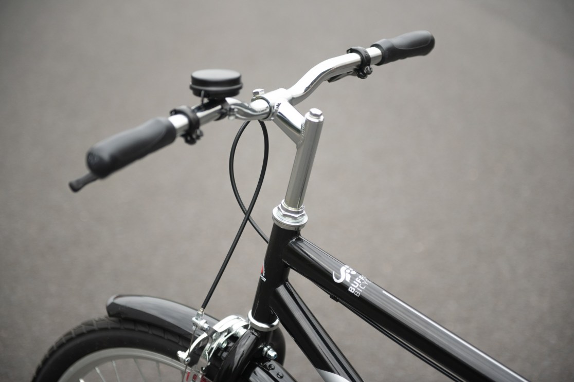 Close-up view of a bicycle's handlebars and frame, featuring black grips and a shiny chrome stem.