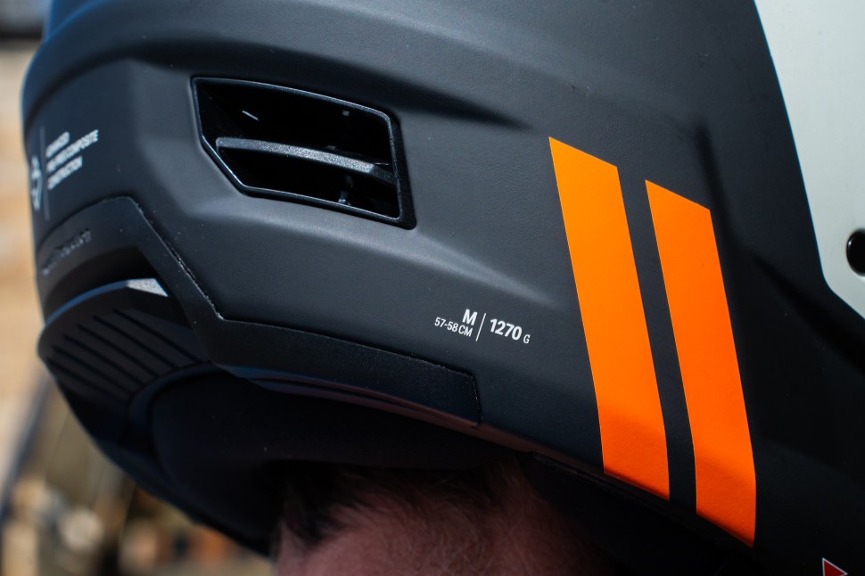Close-up of the Sweet Protection Fixer Composite 2Vi Mips helmet showing black exterior with orange stripes, air vents, and size/weight details.