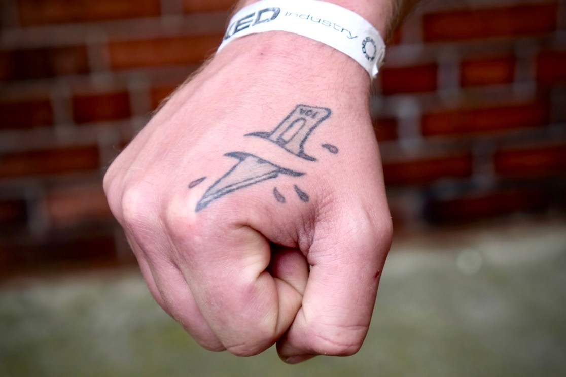 A close-up of a clenched fist with a tattoo of a knife on the back of the hand, showcasing detail in the ink design.