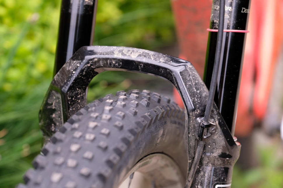 Close-up view of a mountain bike fork featuring a textured surface and a large tire, set against a blurred green background.