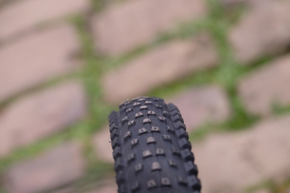 Close-up view of a mountain bike tire tread resting on a cobblestone path.