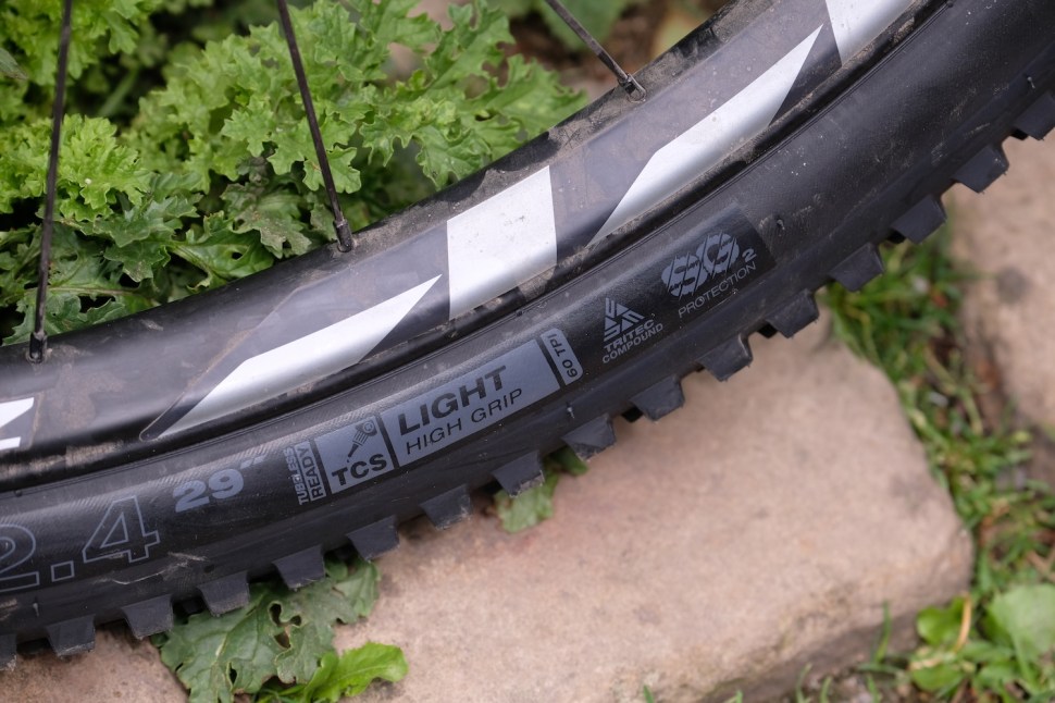 Close-up of a mountain bike tire resting on uneven ground, showcasing its tread pattern and rubber details.
