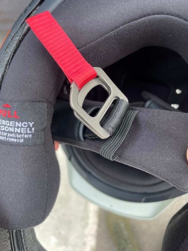 Close-up of the chin strap and interior padding of the Sweet Protection Fixer helmet, featuring a red strap and safety instructions for emergency personnel.